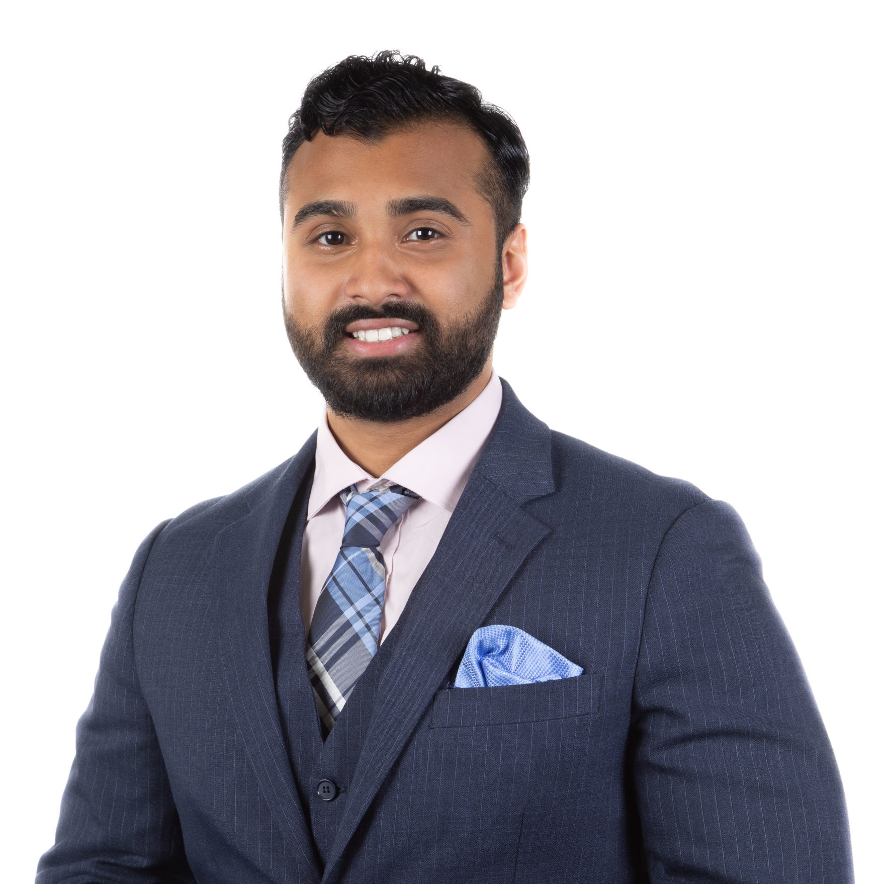 A man wearing a dark blue pinstripe suit, light pink shirt, and plaid tie stands smiling against a plain white background.