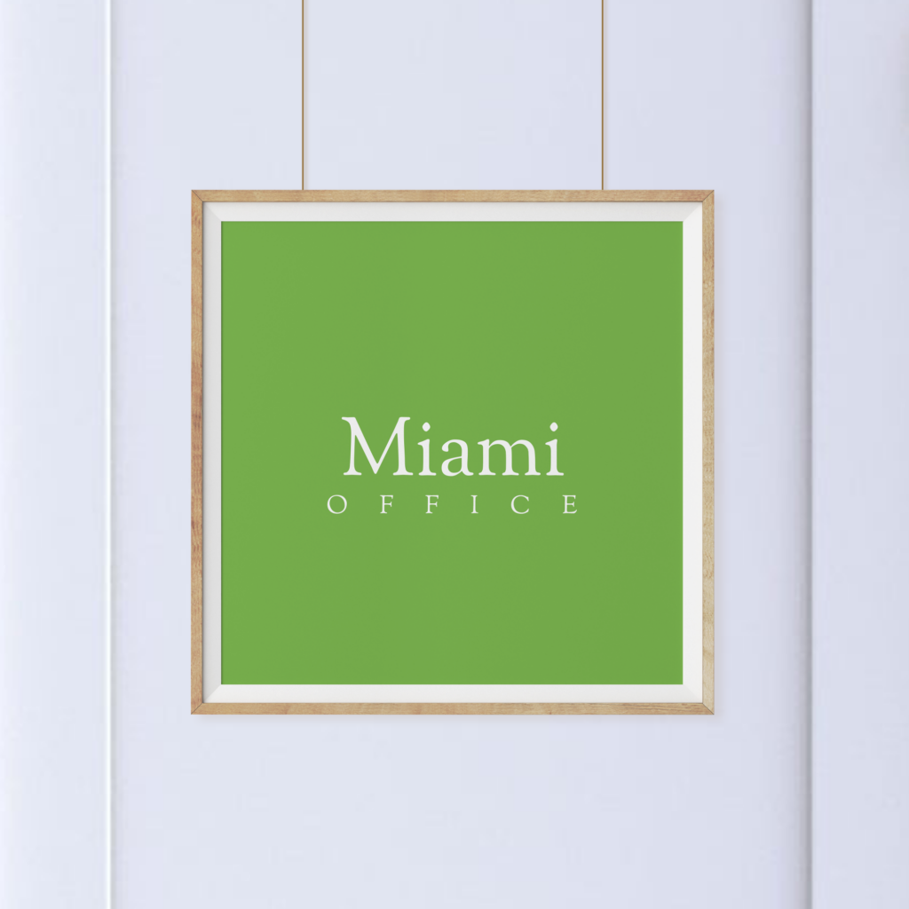 A framed sign with a green background and the words "Miami Office" in white text hangs on a white wall.