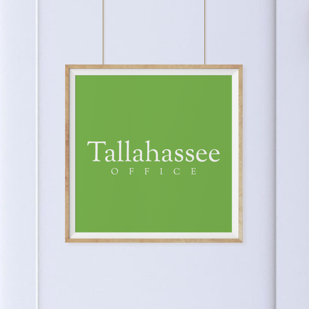 A framed green sign with the words "Tallahassee OFFICE" hangs on a white wall.