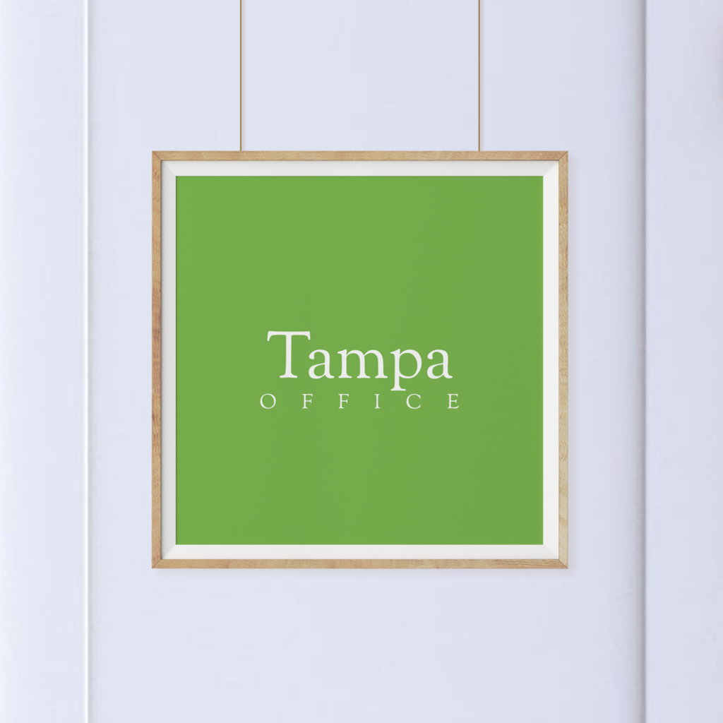 A square green sign with the words "Tampa Office" in white text, framed and hanging on a white wall.