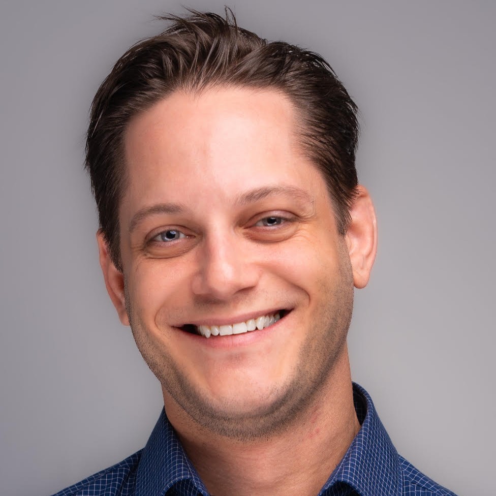 Headshot of a smiling man wearing a blue button-down shirt.