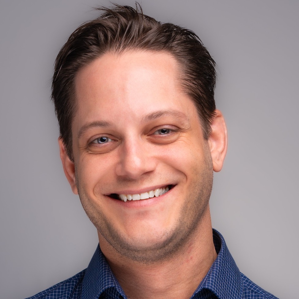Headshot of a smiling man wearing a blue button-down shirt.